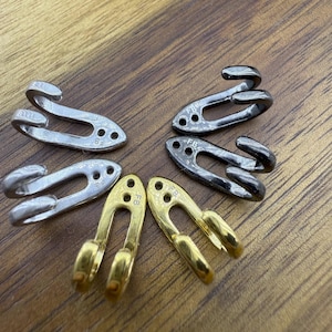 Può includere: Un assortimento di chiusure metalliche in argento, nero e oro. Le chiusure hanno un design a gancio e occhiello, alcune con un gancio curvo. Sono disposte su una superficie di legno.