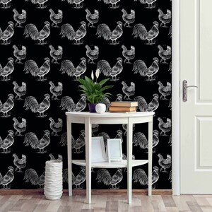 May include: Black and white rooster pattern wallpaper with a white side table and a potted plant. The table has two shelves and a picture frame on the top shelf.
