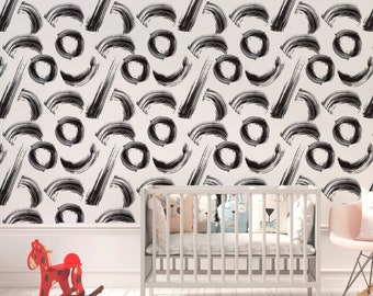 May include: White wallpaper with a repeating pattern of black brushstrokes, including curved lines, circles, and diagonal strokes. A white crib with decorative pillows and a red rocking horse are in the foreground, suggesting a nursery setting.
