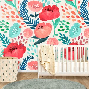 May include: A white crib with a floral patterned wallpaper behind it. The wallpaper features pink, red, and blue flowers with green leaves. A woven basket and a white blanket with gold polka dots are in the foreground.