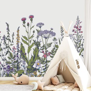 May include: A white teepee tent with a brown floor mat and pillows inside. The teepee is set up in front of a wall with a floral pattern of green leaves and pink, purple, and yellow flowers.