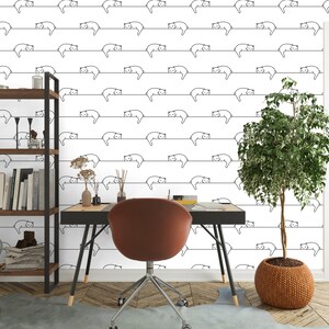 Puede incluir: Una pared blanca con un patr&oacute;n repetitivo de dibujos de l&iacute;nea negra de gatos durmiendo en una l&iacute;nea. Un estante de madera con libros y art&iacute;culos decorativos est&aacute; en el lado izquierdo de la imagen. Un escritorio marr&oacute;n con una silla marr&oacute;n est&aacute; en el medio de la imagen. Una planta verde en maceta est&aacute; en el lado derecho de la imagen.