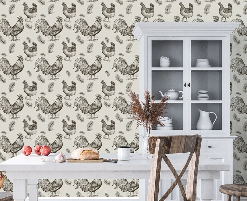 May include: A white kitchen with a white cabinet with glass doors. The cabinet is filled with dishes and a pitcher. The wall behind the cabinet is covered in a wallpaper with a pattern of roosters and feathers.