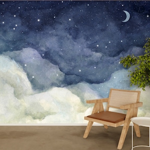 May include: A watercolor painting of a night sky with clouds and stars. A crescent moon is visible in the upper right corner of the image. A wooden chair with a woven seat and a brown cushion sits in front of the painting. A small wooden table with a white top is next to the chair.
