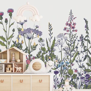 May include: A white wall with a floral wallpaper design featuring a variety of flowers and plants in shades of green, blue, pink, and purple. A white wooden shelf with a toy house, wooden blocks, and a stuffed snail sits in front of the wall.