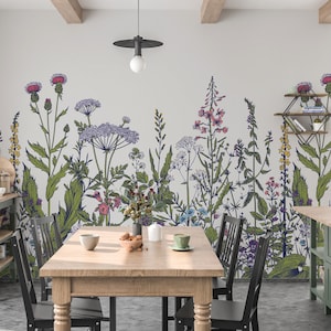 May include: A dining room with a floral wallpaper mural featuring a variety of flowers and plants in shades of green, purple, pink, and yellow. The wallpaper is on the wall behind a wooden table with four black chairs.