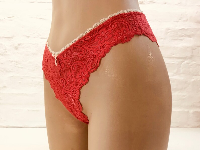 May include: Red lace underwear with a scalloped edge and a small bow detail. The delicate floral pattern and ivory trim create a feminine look. The underwear is displayed on a mannequin.