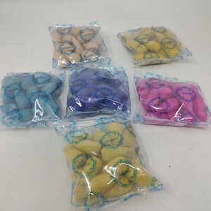 May include: Assortment of colorful, small, sponge-like objects in clear plastic bags. The colors include beige, yellow, blue, purple, and pink. The bags are arranged in a circular pattern, with each bag containing several pieces.