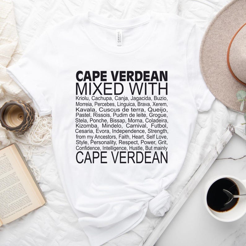 Może przedstawiać: Biały t-shirt z czarnym tekstem, kt&oacute;ry brzmi "Cape Verdean Mixed With" i wymienia r&oacute;żne słowa i frazy związane z kulturą Wysp Zielonego Przylądka. Tekst zawiera "Kriolu, Cachupa, Canja, Jagacida, Buzio, Morreia, Percebes, Linguica, Brava, Xerem, Kavala, Cuscus de terra, Queijo, Pastel, Rissois, Pudim de leite, Grogue, Stela, Ponche, Bissap, Morna, Coladeira, Kizomba, Mindelo, Karnawał, Piłka nożna, Cesaria, Evora, Niepodległość, Siła, od moich przodk&oacute;w, Wiara, Serce, Miłość do siebie, Styl, Osobowość, Szacunek, Moc, Odwaga, Zaufanie, Inteligencja, Praca, Ale przede wszystkim Cape Verdean".
