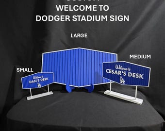 May include: Custom "Welcome to Dodger Stadium" signs in small, medium, and large sizes. The signs are blue and white, with the text "Welcome to Dan's Desk" and "Welcome to Cesar's Desk" on the smaller signs.