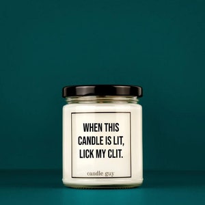 May include: A white candle in a glass jar with a black lid. The candle has a black label with the text "WHEN THIS CANDLE IS LIT, LICK MY CLIT." and the text "candle guy" below the label.