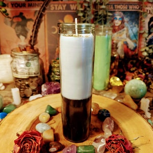 Könnte beinhalten: Eine weiße und schwarze Kerze in einem Glasgefäß mit goldenem Deckel. Die Kerze ist umgeben von bunten Steinen und zwei getrockneten Rosen auf einer Holzoberfläche.