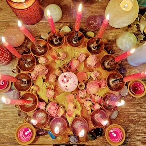 May include: A wooden circle with a variety of dried flowers and leaves in the center.  Around the circle are 13 red candles in small terracotta holders.  There are also several small pink and purple stones around the circle.