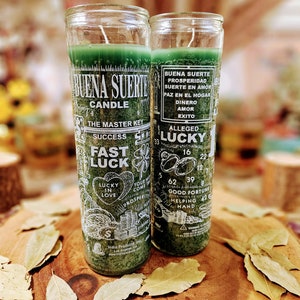 Puede incluir: Dos velas de vidrio verde con las palabras "Buena Suerte Candle" y "The Master Key Success Fast Luck" impresas en ellas. Las velas están decoradas con imágenes de tréboles de cuatro hojas, corazones, monedas y signos de dólares. El texto en las velas está en español e inglés.