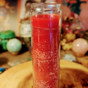 May include: A red glass candle in a clear glass jar. The candle is partially melted and has a textured surface.