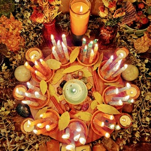 May include: A circular arrangement of lit candles, crystals, and dried leaves on a wooden surface. The scene includes a large orange candle, small candles in terracotta dishes, and a calendar showing February 26, 2026. The website enhergyintentions.com is visible.