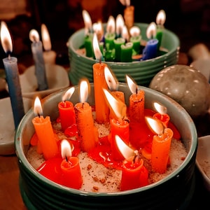 May include: A teal ceramic bowl filled with sand and lit orange candles. The candles are arranged in a circle and are surrounded by melted wax.