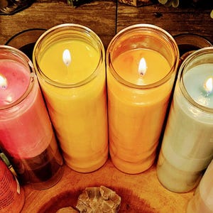 Puede incluir: Seis velas encendidas de colores en tarros de vidrio. Las velas son rojas, rosas, amarillas, naranjas, celeste y blancas. Están dispuestas sobre una superficie de madera, con elementos decorativos.
