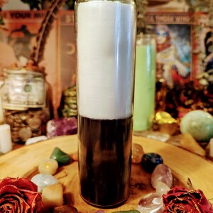 May include: A white and black candle in a clear glass jar. The candle is surrounded by colorful stones and dried roses.