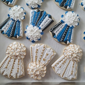 May include: Assortment of decorated sugar cookies with blue and white frosting. The cookies feature the words "Senior", "Guyer", "Alora", "Emme", and "Ava".