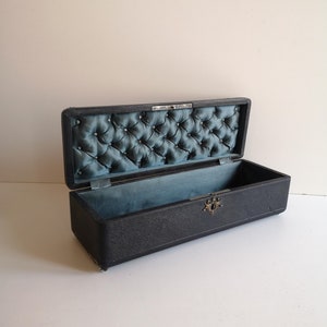 May include: A black rectangular box with a tufted blue velvet lining. The box has a metal clasp and is lined with a blue fabric.