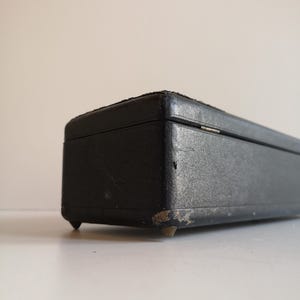 May include: A black rectangular box with a leather-like finish and brass feet. The box has a slightly worn appearance.