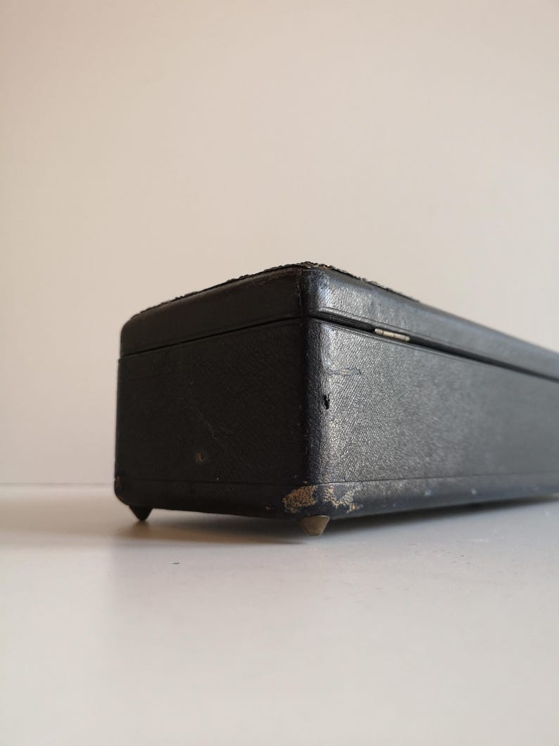 May include: A black rectangular box with a leather-like finish and brass feet. The box has a slightly worn appearance.
