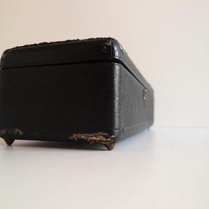 May include: A black rectangular box with a worn leather exterior and gold metal feet. The box is closed and has a slight angle.