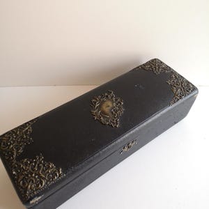 May include: A black rectangular box with ornate gold metal accents and a raised design of a woman's face in the center.