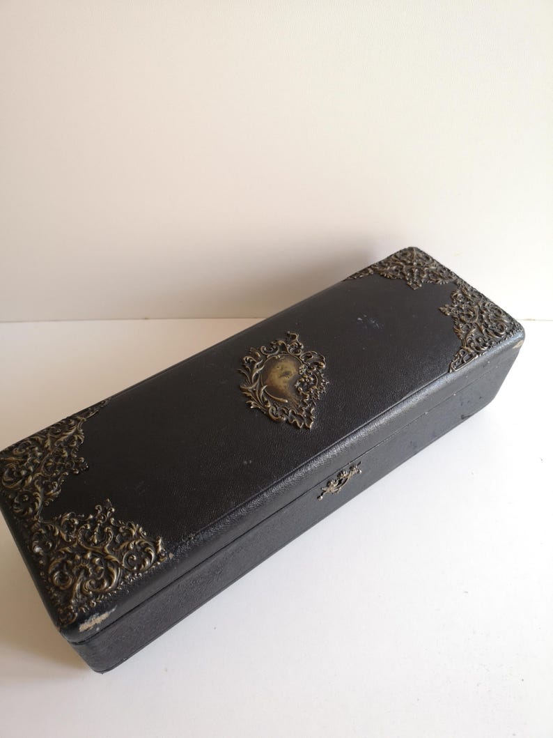 May include: A black rectangular box with ornate gold metal accents and a raised design of a woman's face in the center.