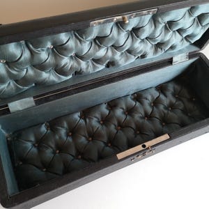 May include: A black rectangular box with a hinged lid. The inside of the box is lined with a blue quilted fabric.