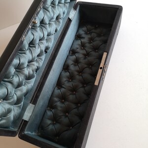 May include: A black rectangular box with a hinged lid. The inside of the box is lined with a dark blue fabric with a tufted pattern.