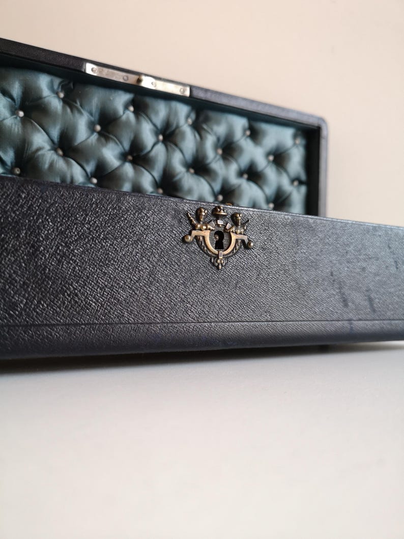 May include: A vintage wooden box with a dark blue leather exterior and a teal blue satin interior. The box has a brass latch with a keyhole and a tufted design on the inside.