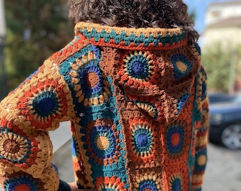 May include: A long, crocheted cardigan with a hood. The cardigan is made of colorful squares with a brown background. The squares feature a variety of colors, including blue, green, orange, and red.