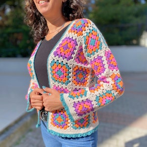 Könnte beinhalten: Eine gehäkelte Strickjacke mit Granny-Square-Muster in den Farben Rosa, Lila, Orange, Türkis und Weiß.