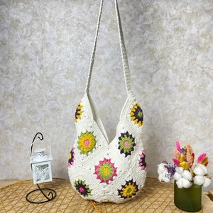 Op de afbeelding: Witte gehaakte tote bag met een bloemenpatroon. De tas heeft een lange band en is gemaakt van een zacht, lichtgewicht materiaal.