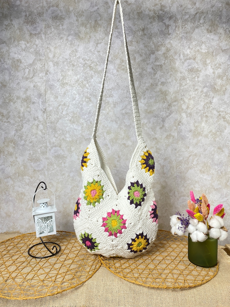Op de afbeelding: Witte gehaakte tote bag met een bloemenpatroon. De tas heeft een lange band en is gemaakt van een zacht, lichtgewicht materiaal.