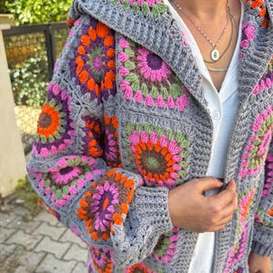 May include: A gray crochet cardigan with a hood, featuring colorful granny square patterns in shades of pink, orange, green, and purple.