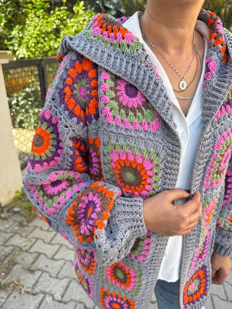 May include: A gray crochet cardigan with a hood, featuring colorful granny square patterns in shades of pink, orange, green, and purple.