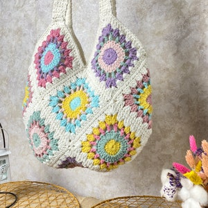 May include: A white crocheted tote bag with a colorful geometric pattern. The bag has a large, open top and two long straps.