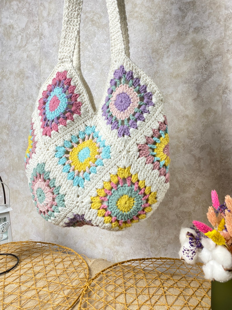 May include: A white crocheted tote bag with a colorful geometric pattern. The bag has a large, open top and two long straps.