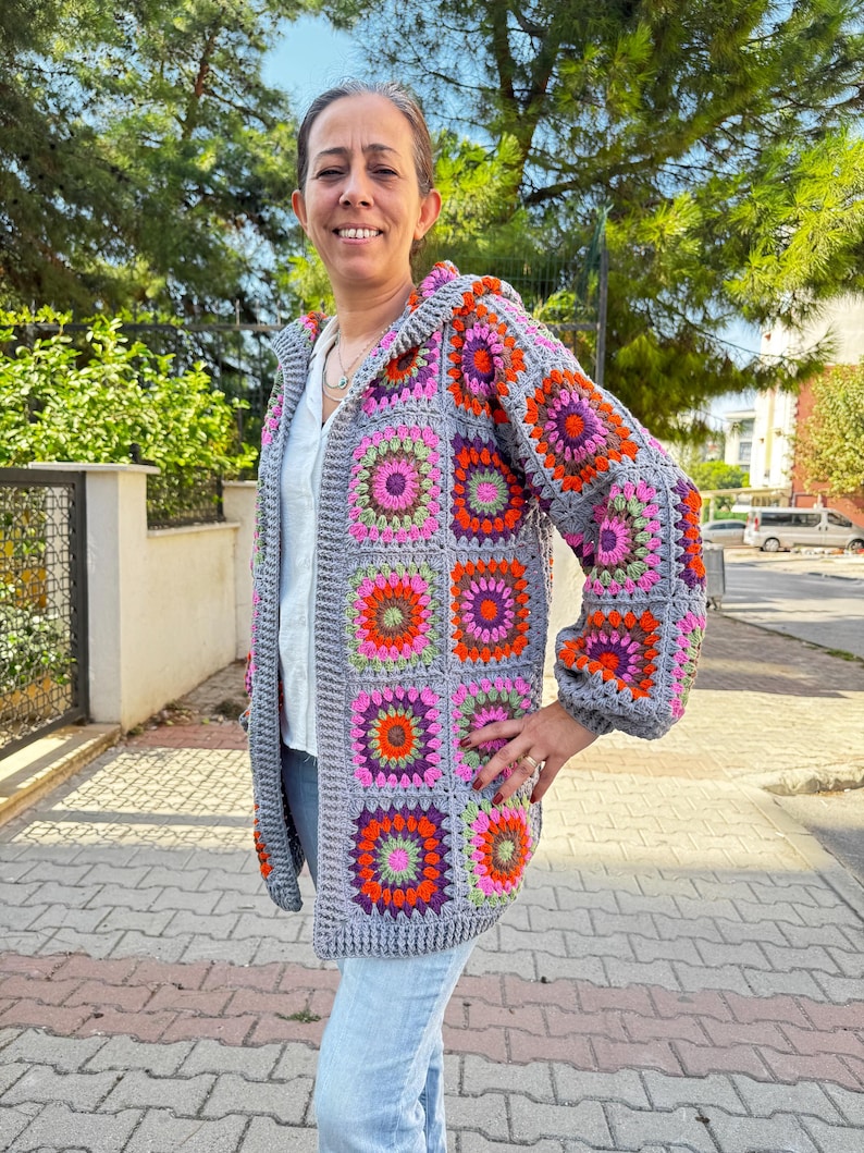 May include: A gray crocheted cardigan with a hood, featuring a colorful geometric pattern of squares with pink, orange, green, and purple accents.