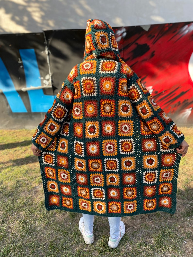 May include: A long, green crocheted cardigan with a hood. The cardigan is made of squares with a colorful pattern of orange, brown, and white.