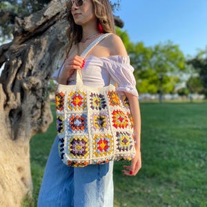 May include: A white crochet tote bag with colorful squares. The bag has a long strap and is made of cotton yarn.