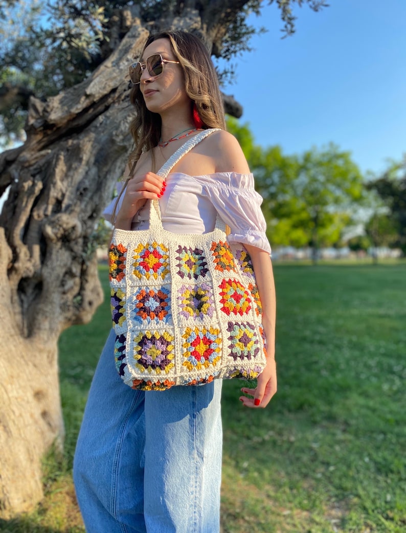 May include: A white crochet tote bag with colorful squares. The bag has a long strap and is made of cotton yarn.