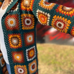 May include: A long, green crochet cardigan with a hood. The cardigan is made of granny squares in various shades of brown, orange, and white.