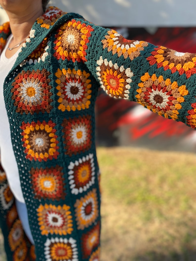 May include: A long, green crochet cardigan with a hood. The cardigan is made of granny squares in various shades of brown, orange, and white.