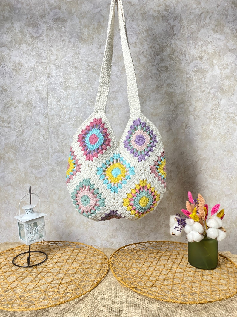 May include: A white crocheted tote bag with colorful floral designs. The bag has a long strap and is made of a soft, textured material.
