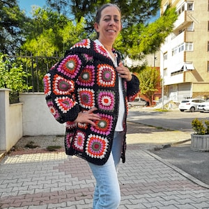 May include: A black crochet cardigan with colorful granny squares. The cardigan has a loose fit and long sleeves.