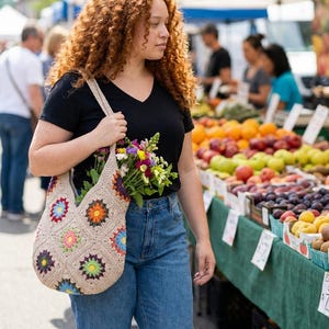May include: A beige crochet tote bag with colourful floral designs, filled with a bouquet of fresh flowers. The bag is carried by a person wearing a black V-neck shirt and blue jeans, at an outdoor market.